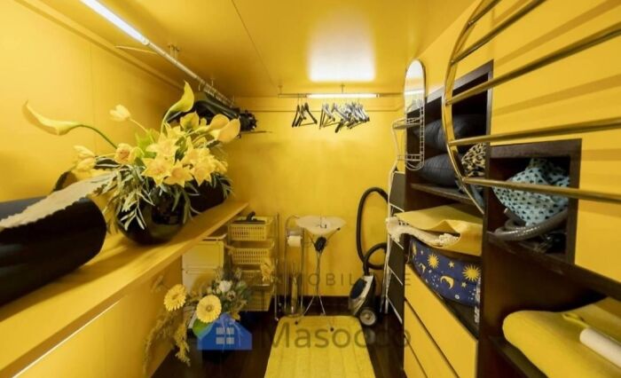 A bright, all-yellow, unhinged real estate listing room with shelves, clothes, and cleaning supplies.