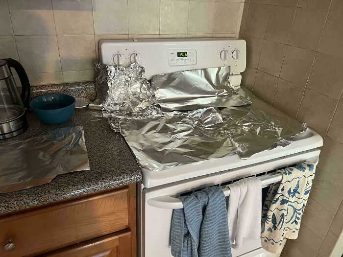 A stove covered in aluminum foil and kitchen items on the counter, showing the messy habits of horrible roommates.