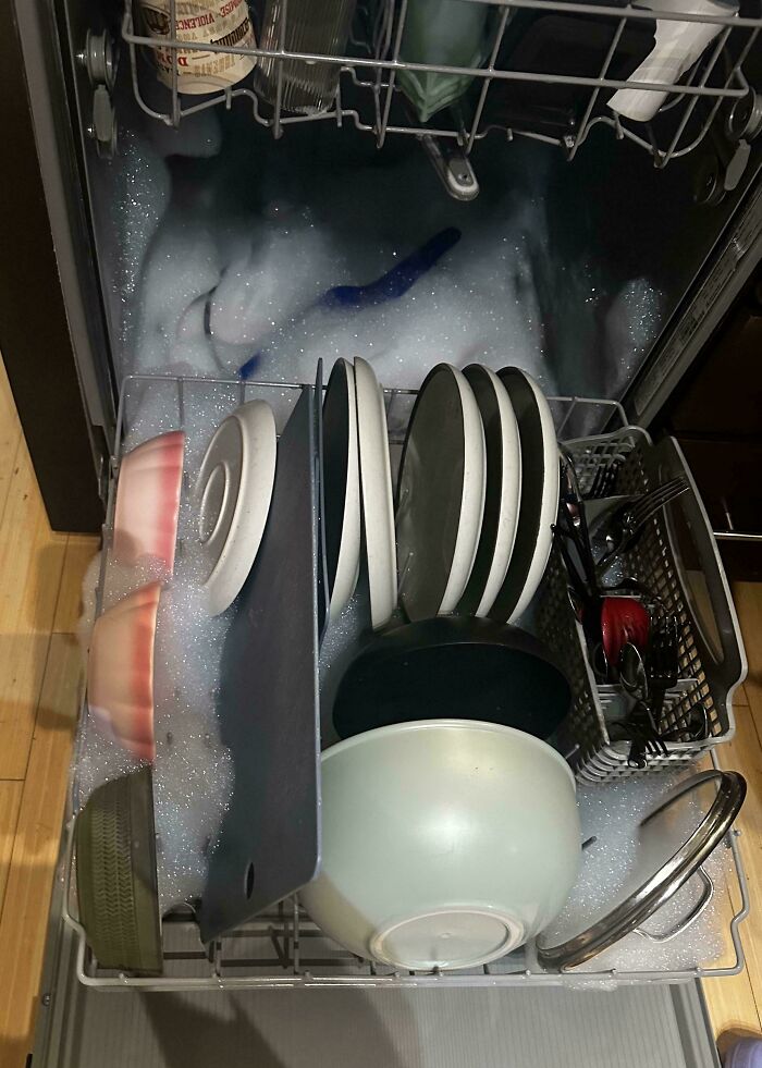 A dishwasher overflowing with soap suds and dishes, a result of a horrible roommate using the wrong soap.