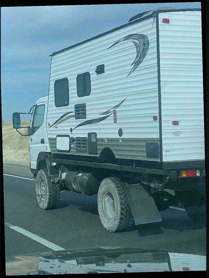 A large white RV trailer attached to an off-road truck, an example of turning junk into clever solutions.
