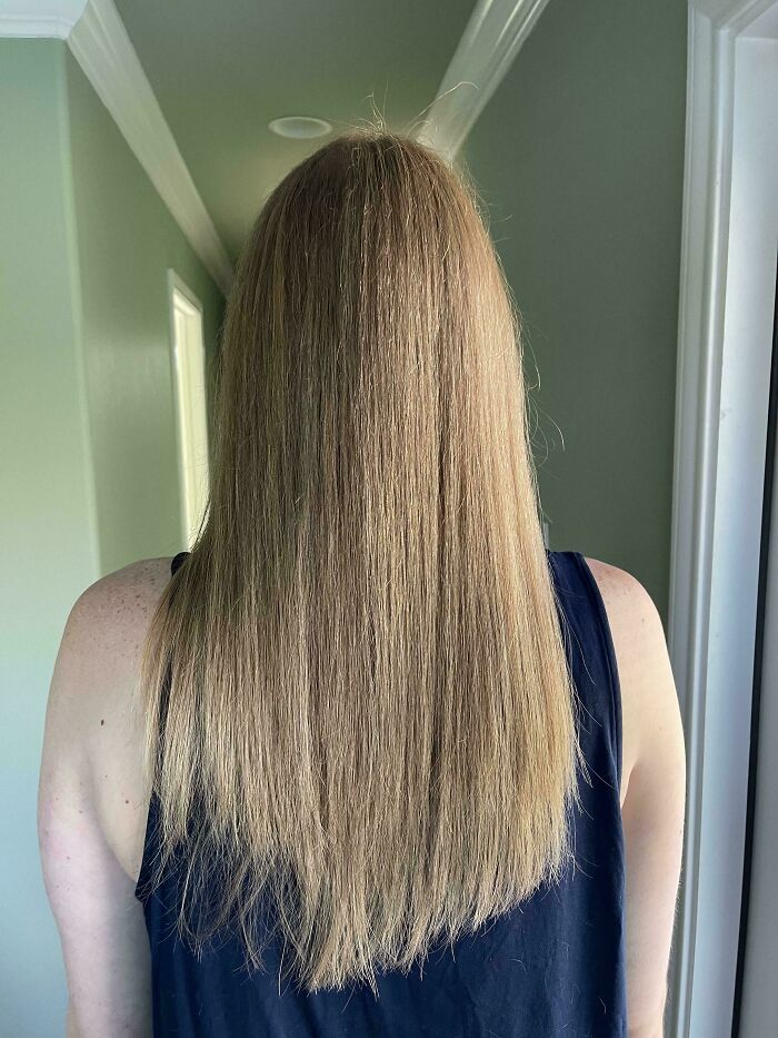 A woman with long, straight, light brown hair looking at hair salon disasters, showing a slightly uneven trim.
