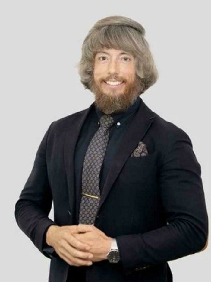 Man with unfortunate haircuts, featuring an unusual bowl cut and beard smiling in a suit.