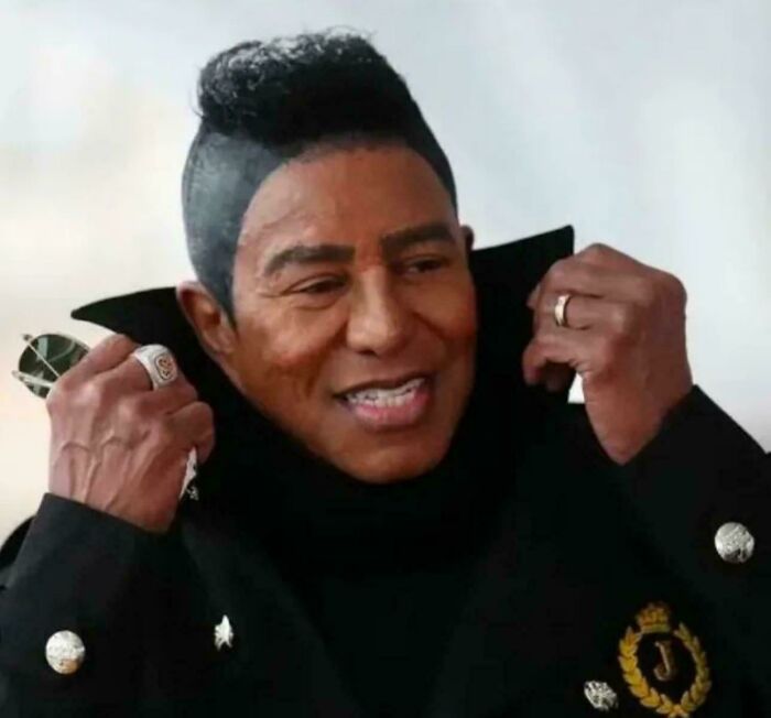 Man with unfortunate haircuts, styled with a distinct faux hawk and shaved sides, smiling.