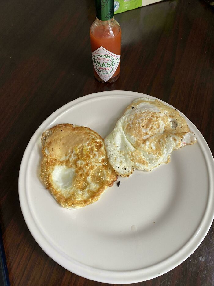 Two poorly cooked fried eggs on a white plate with a bottle of Tabasco sauce, suggesting a horrible roommate's cooking skills.