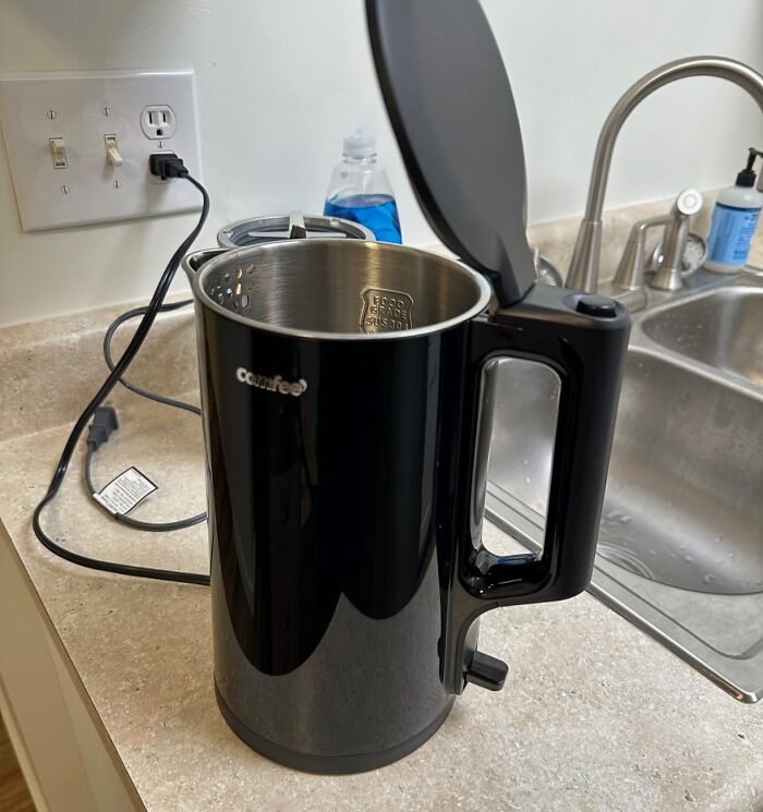 A black Comfee electric kettle on a kitchen counter near a sink, a great Prime Day electronics deal.