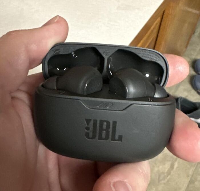 A hand holding a pair of black JBL wireless earbuds in their charging case, a Prime Day electronics deal for your tech.