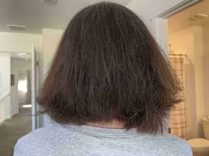 A woman with short, dark brown hair looking at hair salon disasters, showing a poorly cut bob.