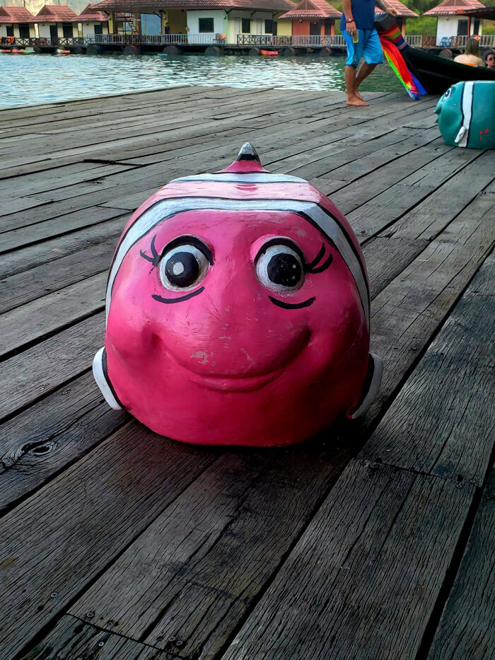 A pink fish-shaped buoy with a smiling, yet creepy, face on a wooden dock, a design fail.