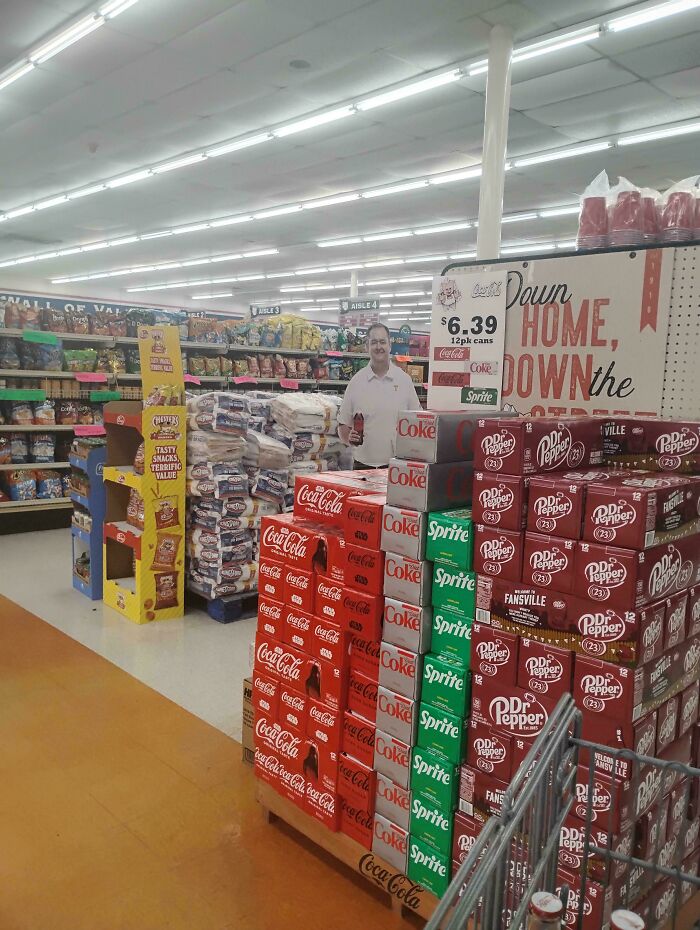 A man in a supermarket aisle filled with soda displays, a design fail due to overwhelming product placement.