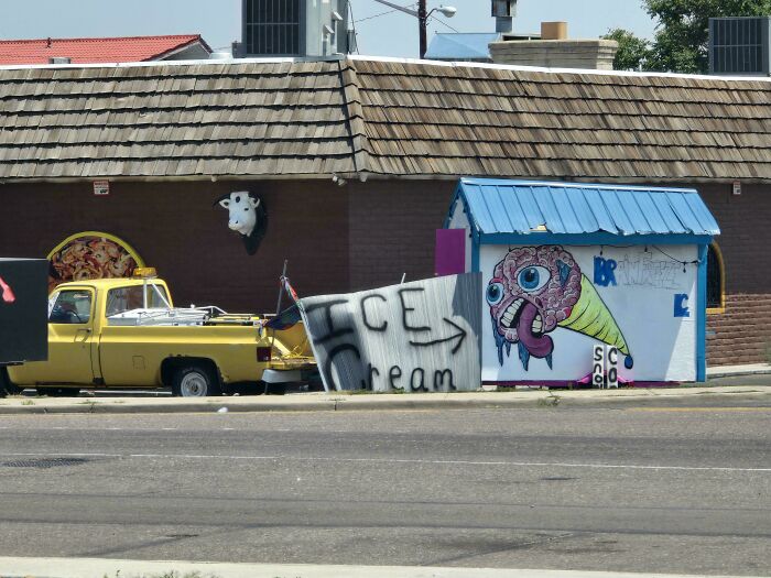 A yellow pickup truck and a building with a cow head sculpture and an ice cream stand with a creepy design fail.