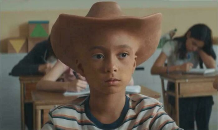 A young boy wearing an oversized cowboy hat in a classroom, a creepy design fail.