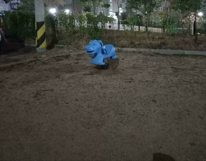 A blue spring rider shaped like a hippopotamus in a sandy playground, a creepy design fail.