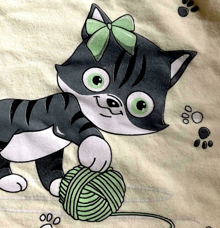 A close-up of a cartoon gray tabby kitten with green eyes and a green bow playing with a green yarn ball. This image shows a design fail.