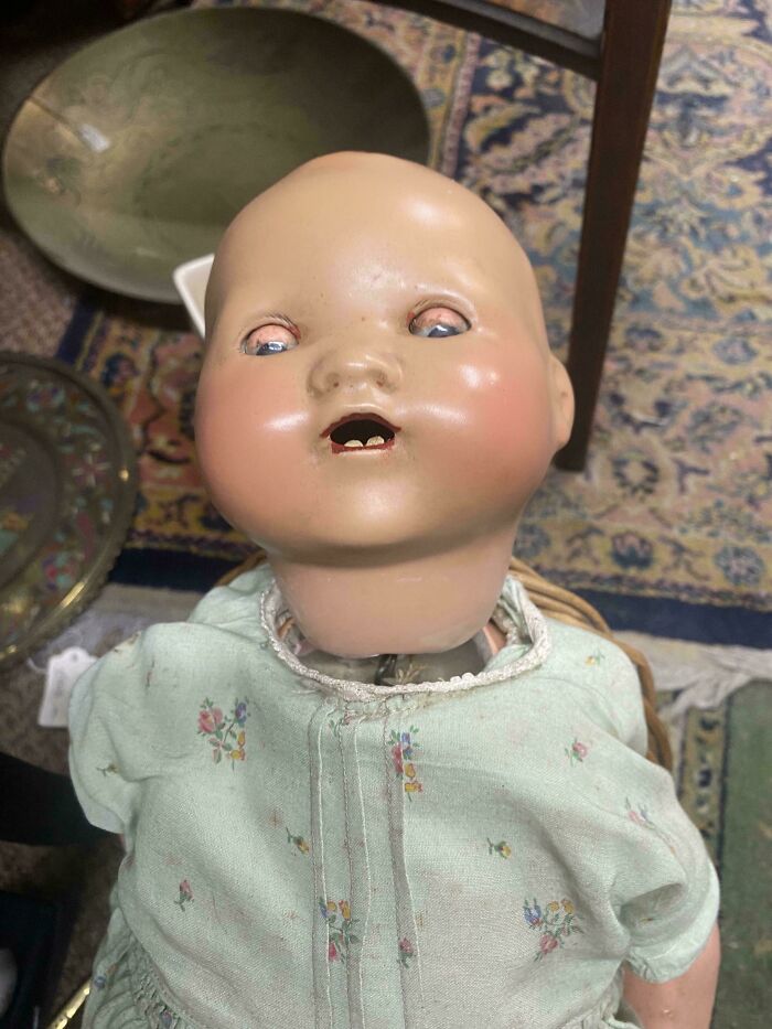 A unsettling antique baby doll with a pale, bald head and wide eyes, a creepy design fail.