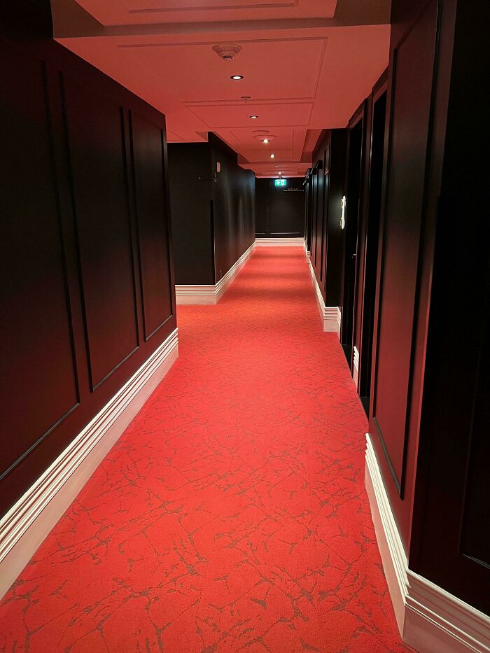 A dimly lit hotel hallway with red carpet, a design fail that makes people feel uncomfortable.