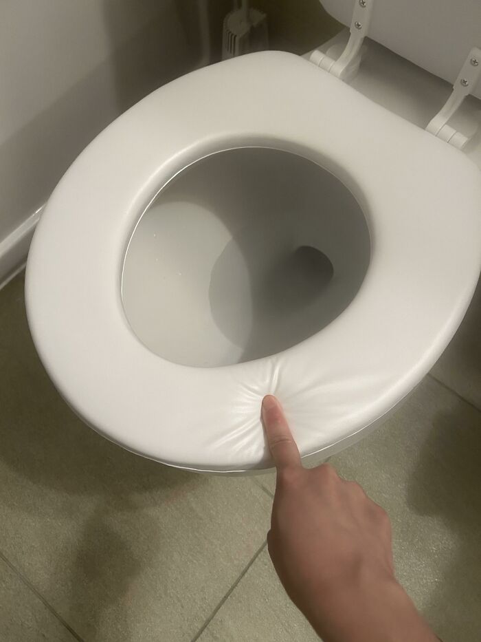 A close-up of a finger pressing down on a wrinkled, ill-fitting toilet seat, indicative of horrible landlords and a tenant's miserable life.