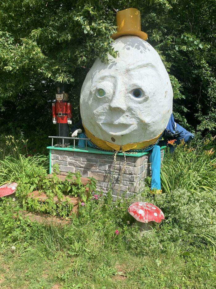 A Humpty Dumpty statue, a creepy design fail with a strange face in a garden.