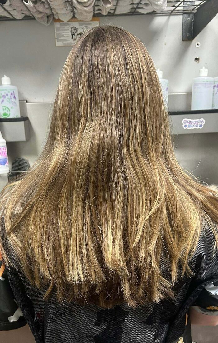 A woman with long, light brown hair looking at hair salon disasters, showing uneven highlights and dry ends.