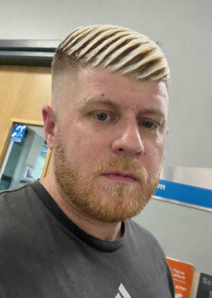 A man with a blonde, striped, unfortunate haircut and a ginger beard looks directly at the camera.