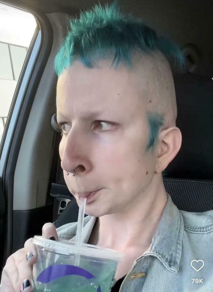 Person with an unfortunate haircut, bright blue hair in a short mohawk, drinking from a cup.