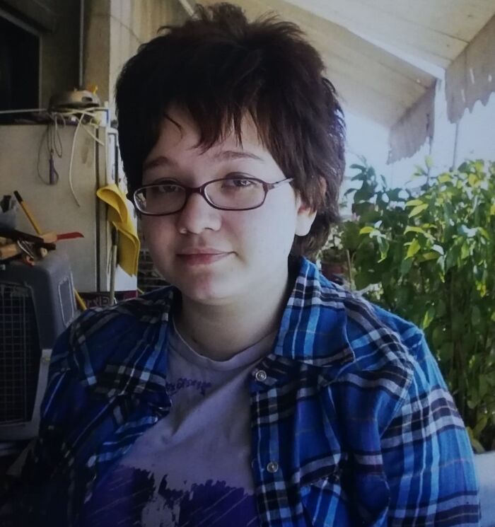 A person with a hair salon disaster, sporting an uneven short haircut and glasses, looking at the camera.