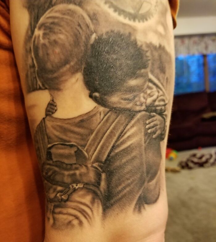 A black and white tattoo depicting a person holding a small child in their arms, showcasing adoption stories.