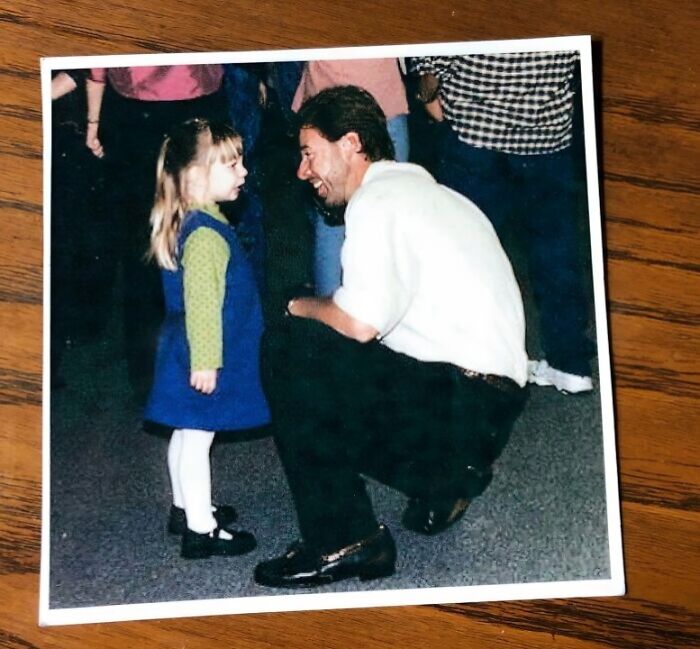 A man kneeling and smiling at a young girl, both looking at each other, captured in a heartwarming adoption story moment.