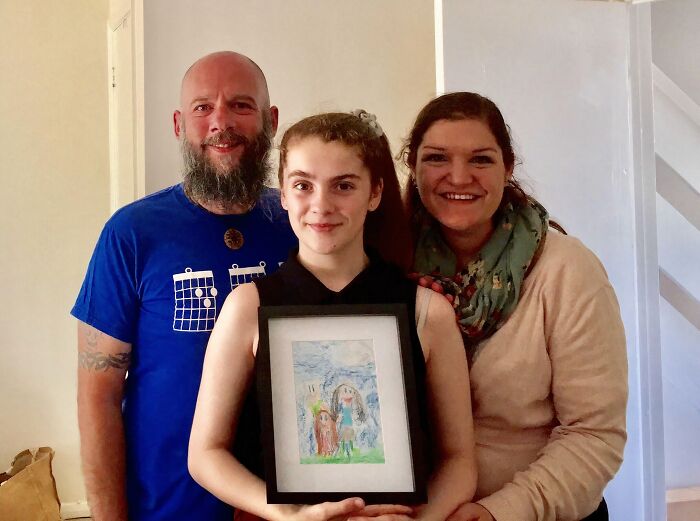 Smiling parents with their adopted daughter holding a framed drawing, illustrating positive adoption stories and chosen families.
