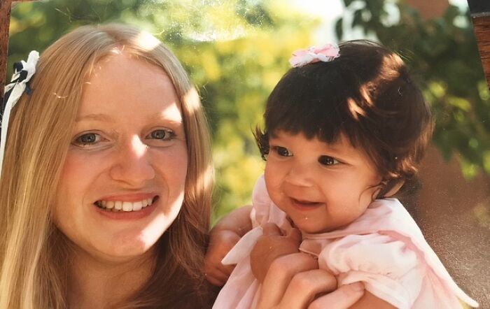 A happy adoption story showing a blonde woman holding a smiling baby with a pink bow in her hair.