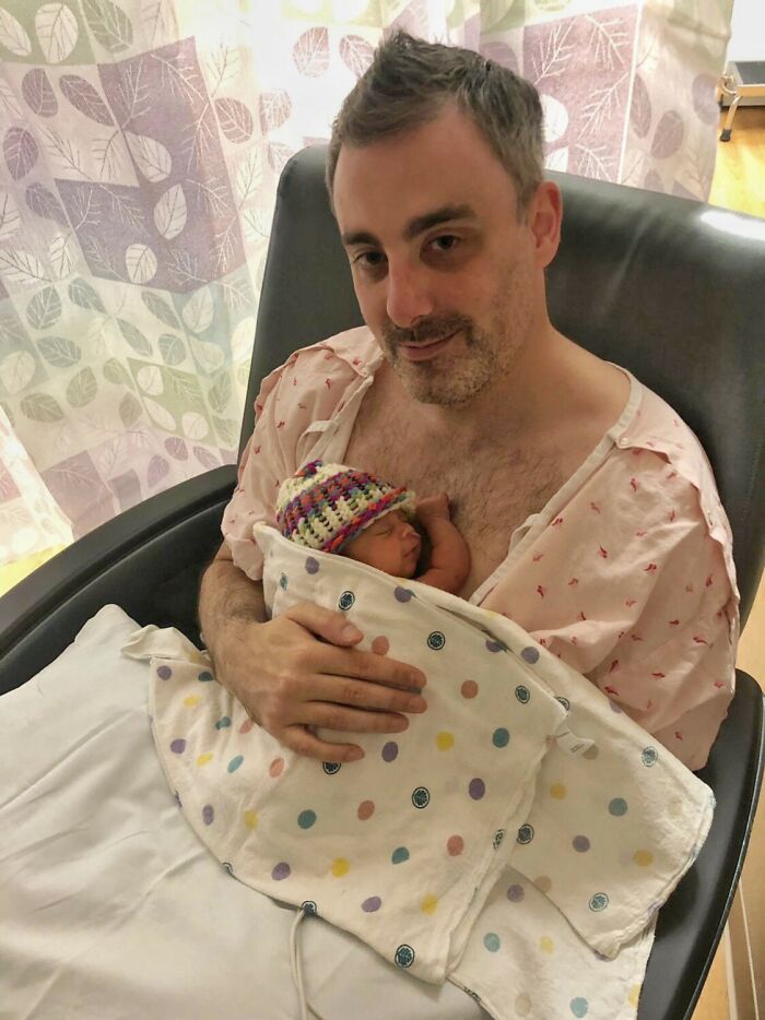 A man in a hospital gown holding a newborn baby wrapped in a polka-dotted blanket, a tender moment from an adoption story.