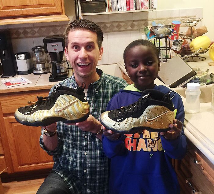 A father and his adopted son smiling and holding up matching sneakers, depicting joyful adoption stories.