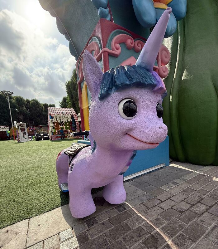 A creepy unicorn ride, a design fail that makes people feel uncomfortable, in an outdoor amusement area.