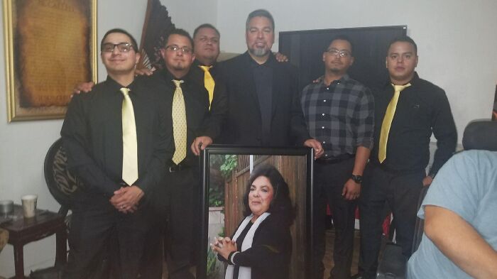 A group of men posing with a framed photo of a woman, representing cherished memories and strong families from adoption stories.