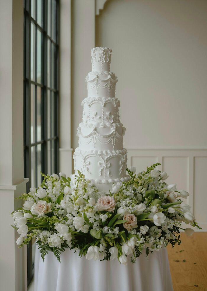 An amazing baker's treat: a towering white wedding cake surrounded by fresh white and pink flowers.