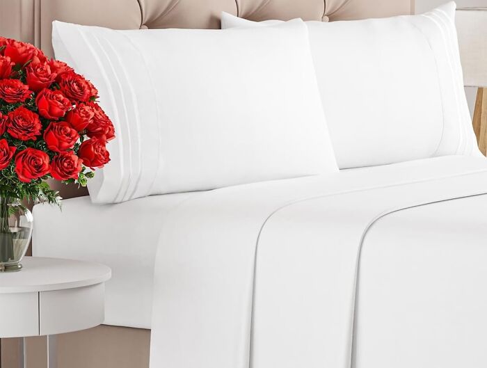 A neatly made bed with white sheets and pillows, accompanied by a vase of red roses, a top home find.