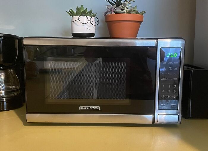 A BLACK+DECKER microwave, a useful kitchen find on Prime Day, sits on a counter with two potted succulents.