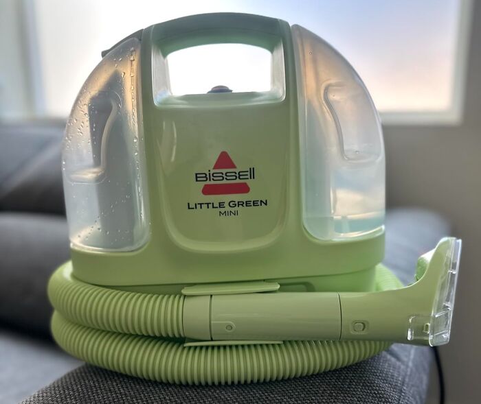 A green Bissell Little Green Mini cleaner, a practical home find on Prime Day, sits on a gray couch.