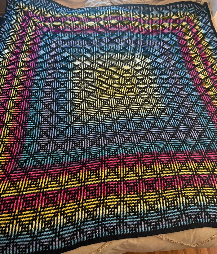 An incredible, colorful crochet blanket with a geometric pattern of squares and vibrant stripes, made by a crochet enthusiast.