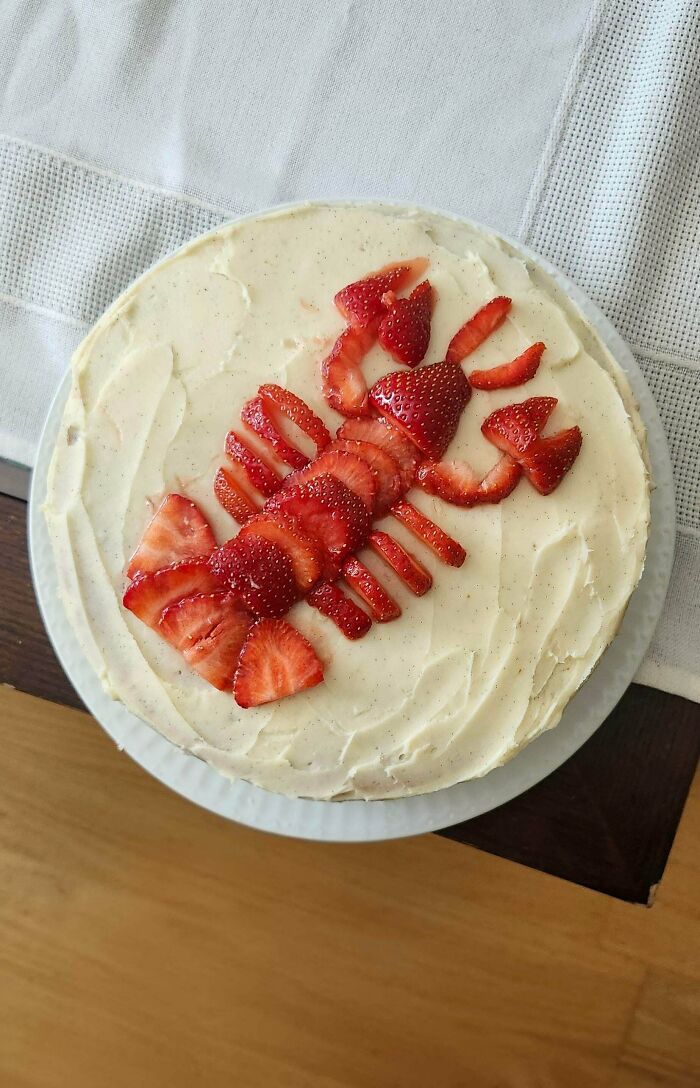 A delicious baker's treat cake with white frosting, decorated with strawberries arranged like a lobster.