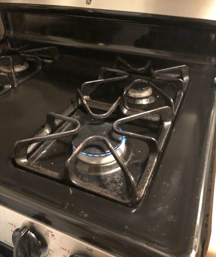 A close-up of a dirty stove with a lit burner, demonstrating how horrible roommates neglect household chores.