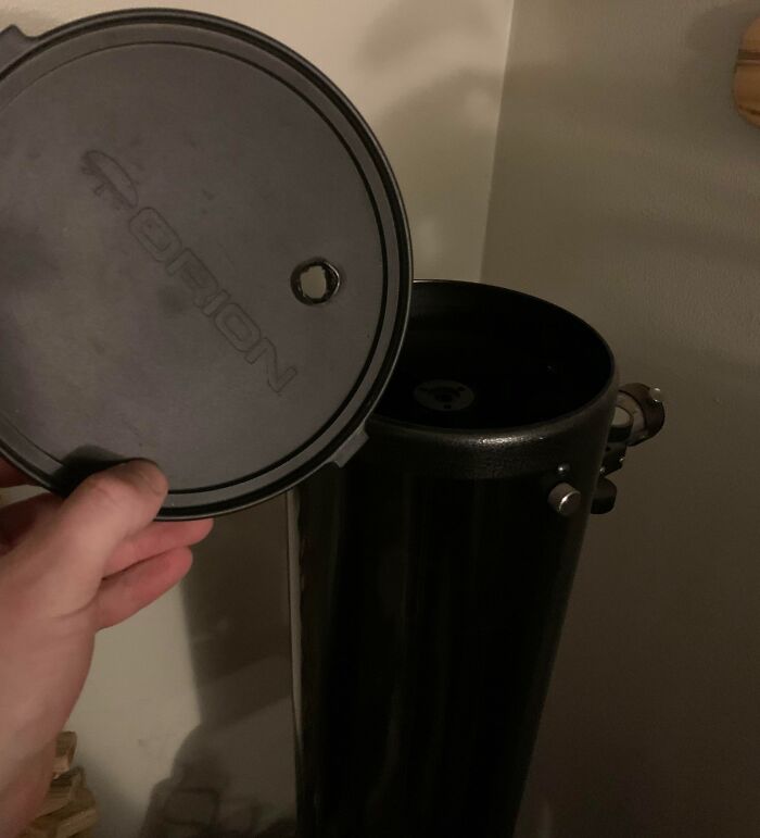 A hand holding a lid off a black tube, revealing what appears to be a scope, stored improperly by a horrible roommate.