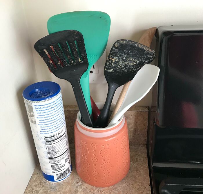 A close-up of a counter with a container full of dirty kitchen spatulas, evidence of a horrible roommate.