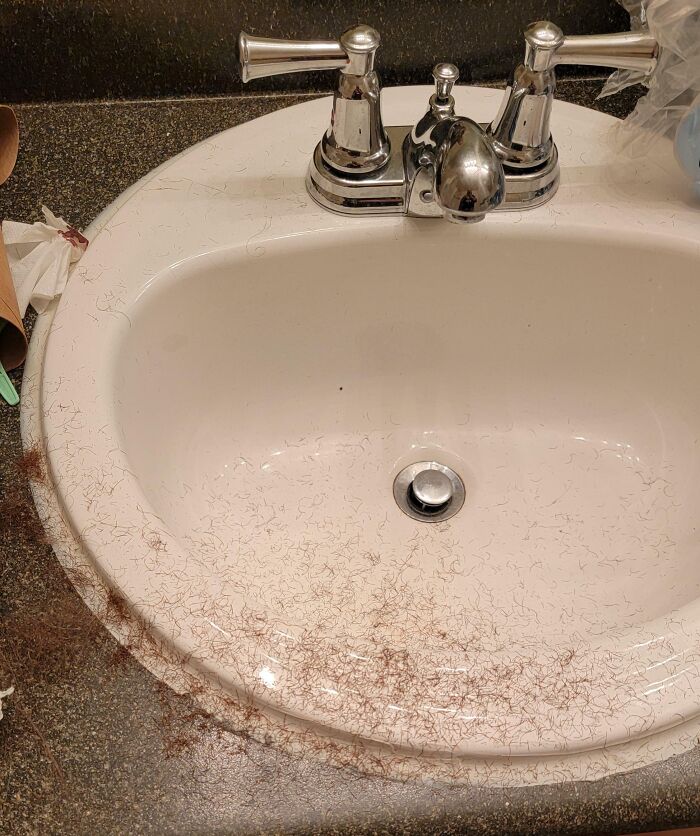 A bathroom sink covered in a large amount of brown hair clippings, a typical scene left by horrible roommates.