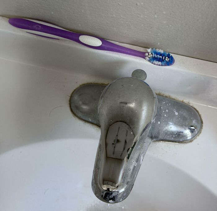 A dirty toothbrush near a calcified faucet in a sink, highlighting a horrible roommates unsanitary habits.