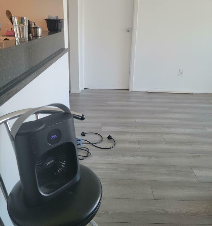 A small fan on a chair in a sparse room, reflecting a horrible roommate's minimalist or messy living conditions.
