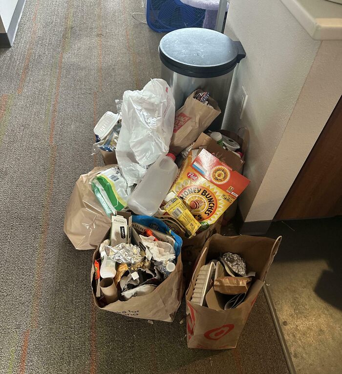 Several overflowing bags of trash and recycling, including cereal boxes, piled on a carpet by horrible roommates.