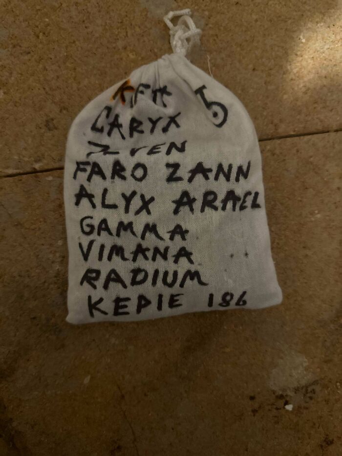 A small white cloth bag with several names written in black marker, resting on a textured surface, one of the many things that should be left alone.