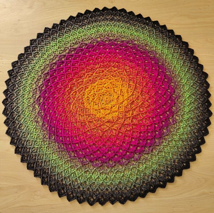 An incredible, vibrant circular crochet piece with a gradient of pink, orange, green, and black, created by a crochet enthusiast.