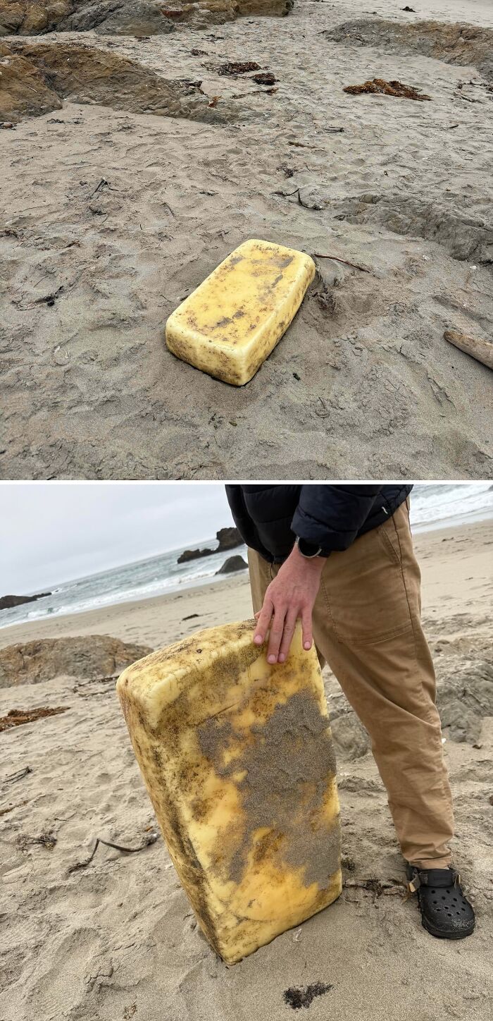 A person on a beach handling a large, yellow, rectangular object covered in sand; things that should be left alone.