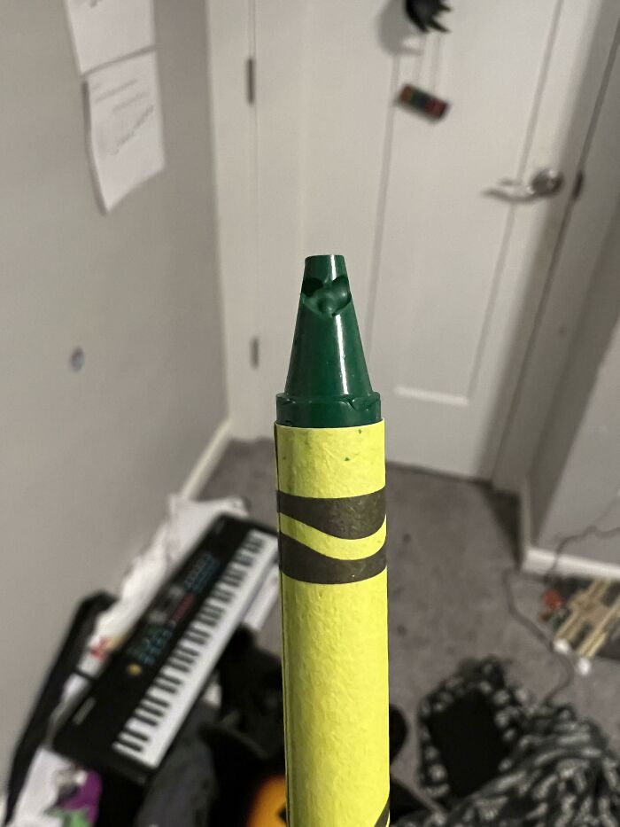 A close-up of a green and yellow crayon with a heart-shaped tip, a weird and wholesome detail.
